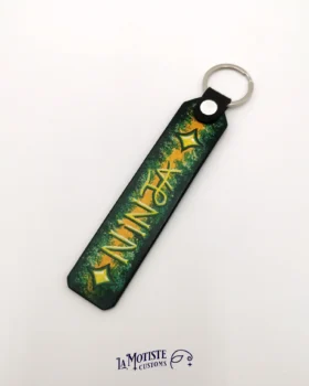Porte-clés en cuir peint à la main Ninja. Le porte clés a un fond dégradé de noir à l'extérieur à orange au centre et le mot NINJA est peint en jaune par dessus, entouré de 2 étoiles à 4 branches