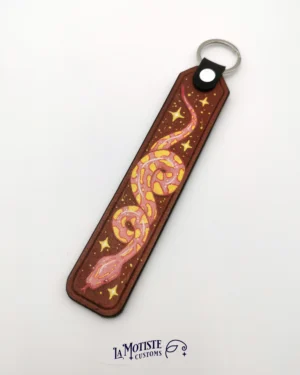 Porte-clés en cuir peint à la main. Base de cuir naturel texturé. Le motif est un python rose à tâches jaunes qui forme des volutes avec son corps, entouré de quelques étoiles jaunes.