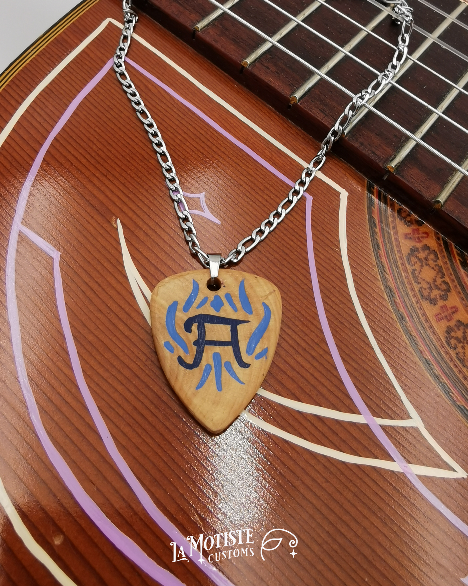 Photo du collier médiator initiale A. Le médiator est en bois de buis, le A en lettrage fin bleu marine et les ornements qui l'entourent en bleu. Fabe B